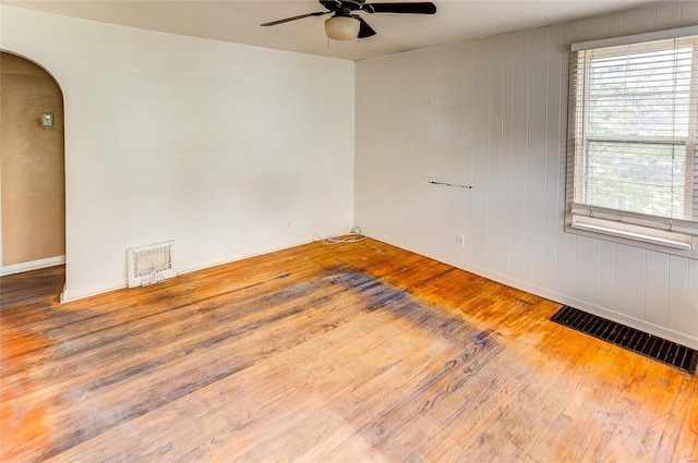 empty room featuring arched walkways, a ceiling fan, wood finished floors, and visible vents