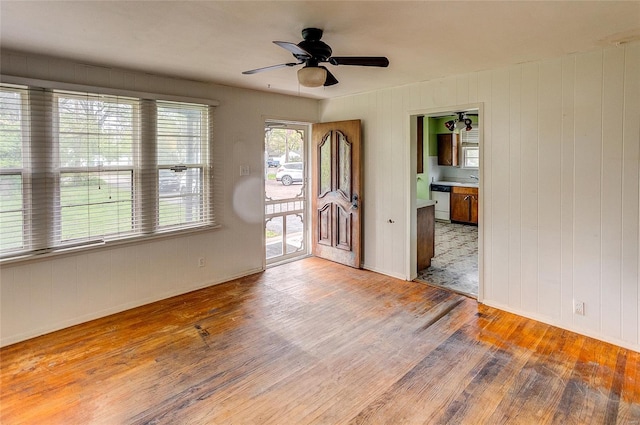 empty room with baseboards, ceiling fan, wood walls, and wood finished floors