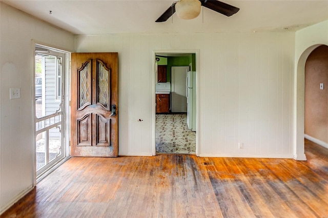 spare room with arched walkways, baseboards, a ceiling fan, and wood finished floors