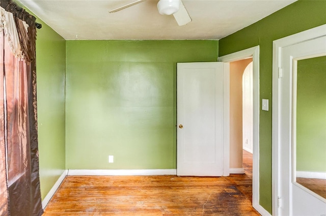 unfurnished bedroom featuring baseboards, a ceiling fan, arched walkways, and wood finished floors