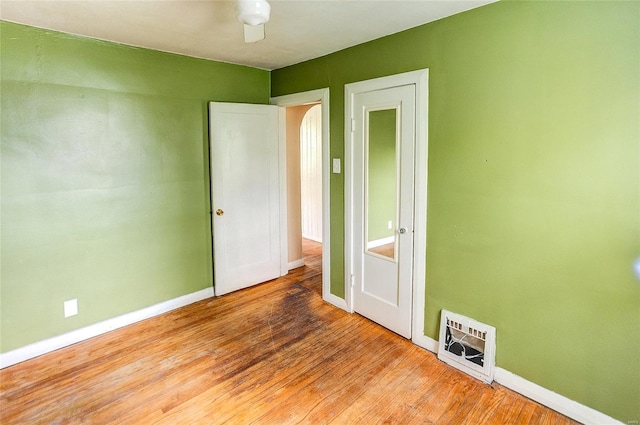 unfurnished bedroom with baseboards, arched walkways, wood finished floors, and visible vents