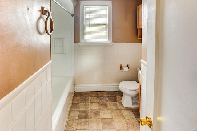 bathroom featuring stone finish floor, a wainscoted wall, toilet, and shower / washtub combination