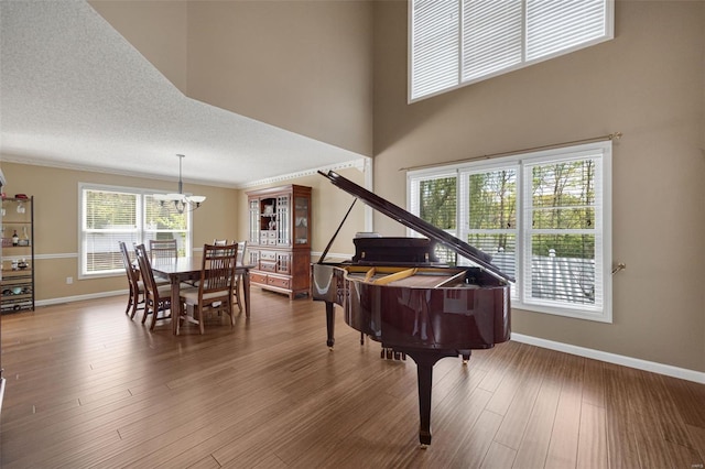 sitting room with crown molding, wood finished floors, baseboards, a notable chandelier, and a high ceiling