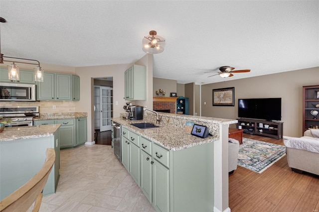 kitchen with appliances with stainless steel finishes, a sink, a peninsula, open floor plan, and green cabinets