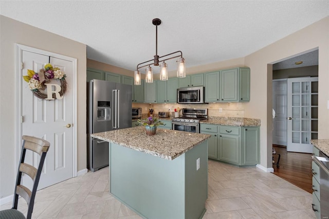 kitchen featuring light stone countertops, stainless steel appliances, decorative backsplash, pendant lighting, and green cabinets