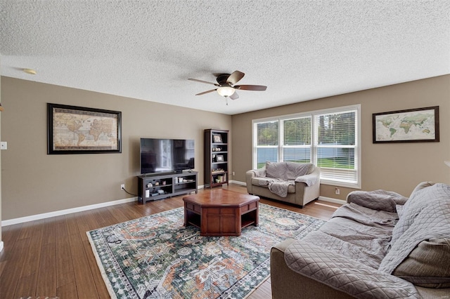 living area featuring baseboards, ceiling fan, a textured ceiling, and wood finished floors