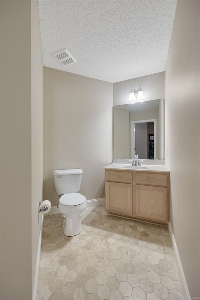 bathroom with vanity, toilet, a textured ceiling, baseboards, and visible vents