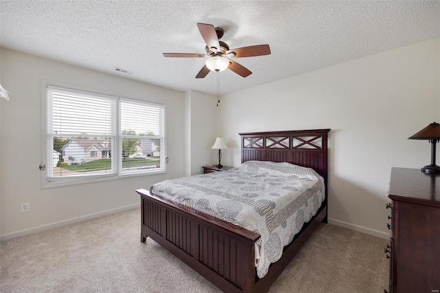 bedroom featuring light colored carpet, a textured ceiling, a ceiling fan, baseboards, and visible vents