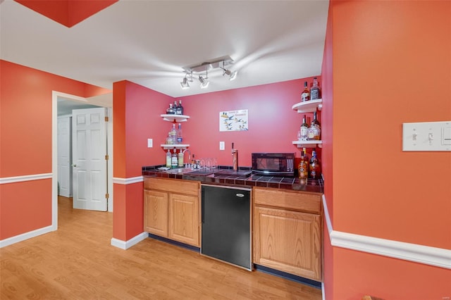 bar with black microwave, light wood-style flooring, refrigerator, and wet bar