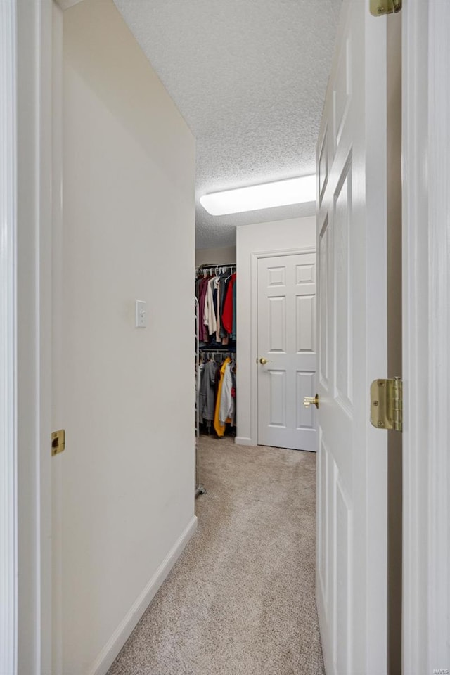 corridor with carpet floors, a textured ceiling, and baseboards