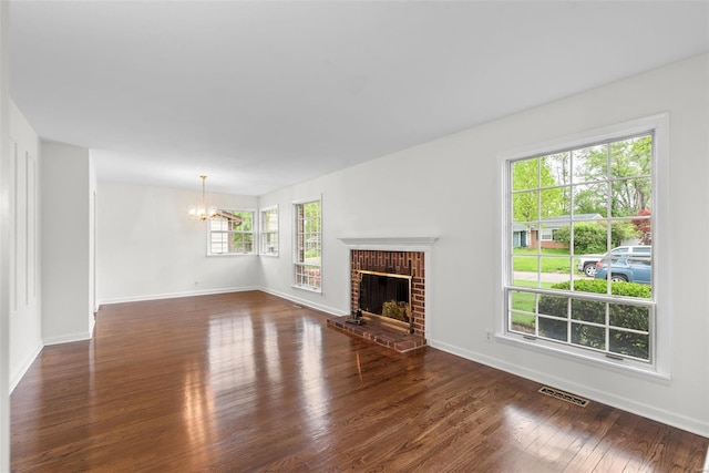 unfurnished living room featuring visible vents, an inviting chandelier, a brick fireplace, baseboards, and dark wood-style floors