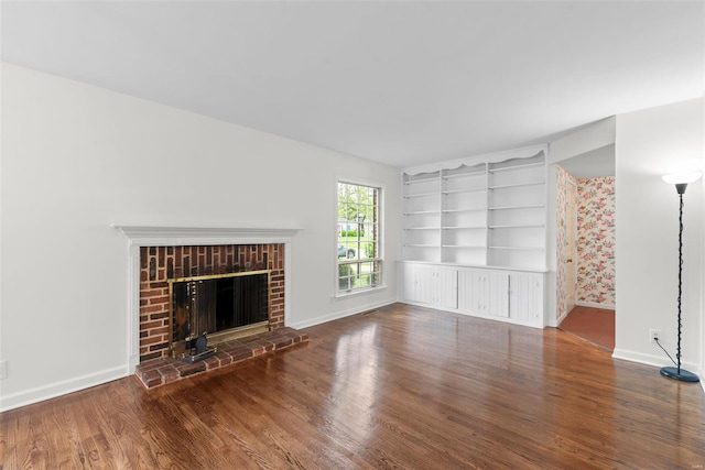 unfurnished living room with baseboards, a brick fireplace, wood finished floors, and built in shelves