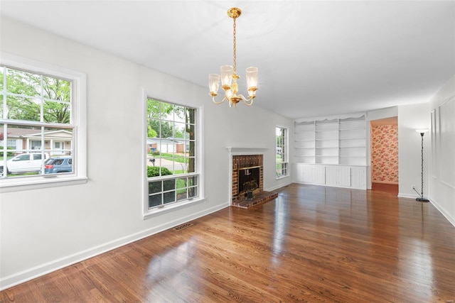 unfurnished living room with visible vents, built in features, wood finished floors, baseboards, and a notable chandelier