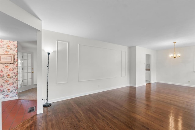 unfurnished living room featuring baseboards, visible vents, wood finished floors, and a notable chandelier