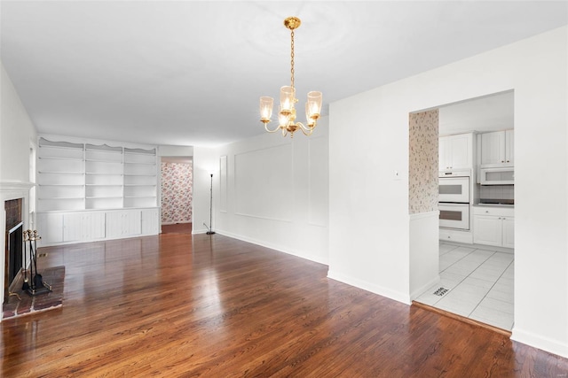 unfurnished living room with a brick fireplace, an inviting chandelier, built in shelves, and light wood-style flooring