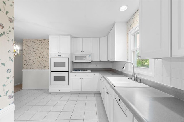 kitchen with a sink, baseboards, white cabinets, wallpapered walls, and white appliances