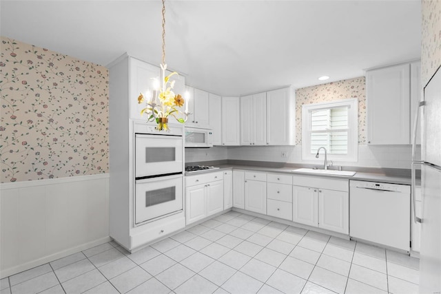 kitchen with a sink, wainscoting, white appliances, and wallpapered walls
