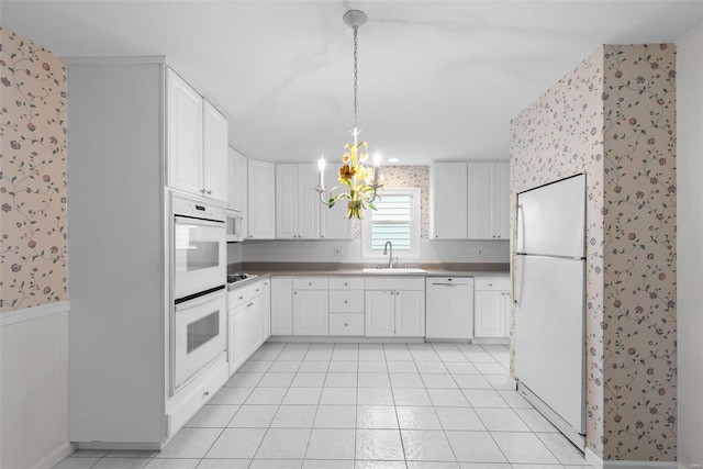 kitchen with an inviting chandelier, white appliances, wallpapered walls, white cabinets, and a sink