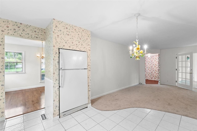 unfurnished dining area with baseboards, a notable chandelier, light carpet, and wallpapered walls