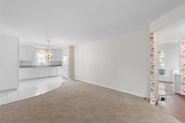unfurnished living room featuring a sink, visible vents, light carpet, and a wealth of natural light