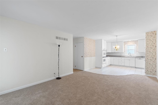 unfurnished living room featuring light carpet, a sink, baseboards, wallpapered walls, and visible vents
