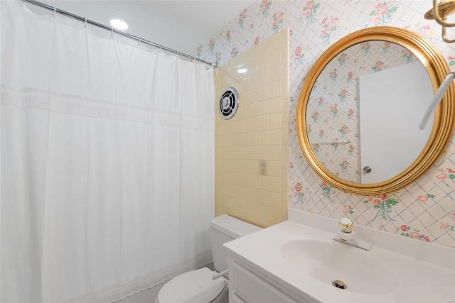 bathroom with tile walls, curtained shower, vanity, toilet, and wallpapered walls