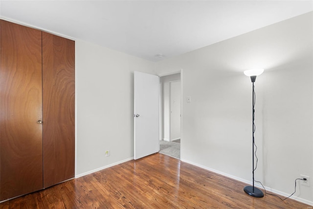 unfurnished bedroom featuring baseboards, wood finished floors, and a closet