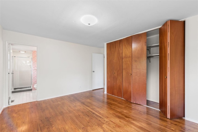 unfurnished bedroom featuring connected bathroom, baseboards, wood finished floors, and a closet