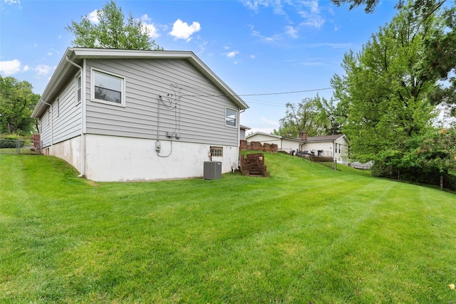 rear view of house featuring central air condition unit, fence, and a yard