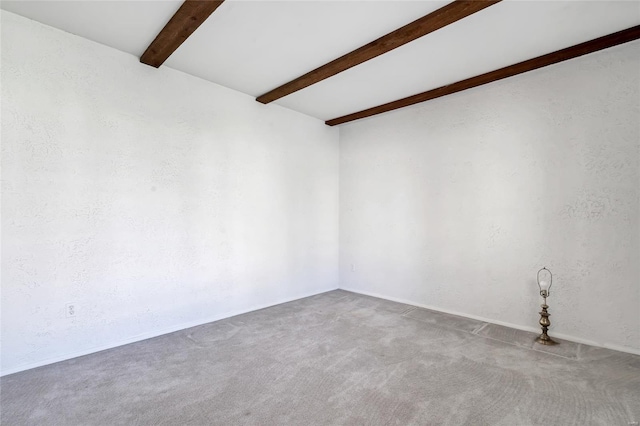 carpeted spare room featuring a textured wall and beamed ceiling