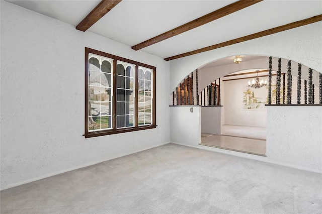 carpeted spare room with beamed ceiling, an inviting chandelier, and a textured wall