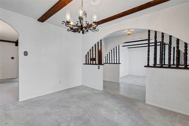 carpeted spare room featuring a textured wall, arched walkways, a notable chandelier, and beam ceiling