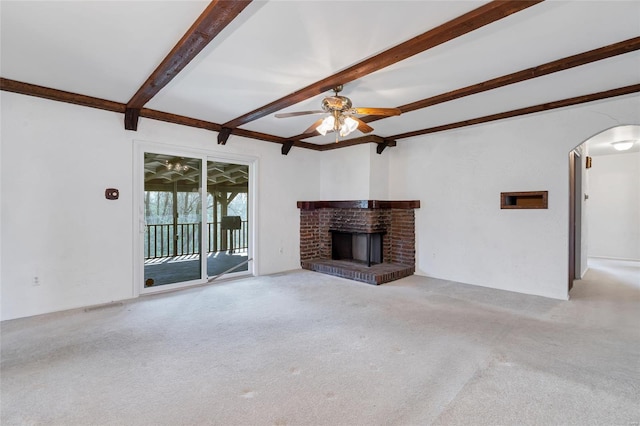 unfurnished living room with arched walkways, ceiling fan, beam ceiling, and carpet