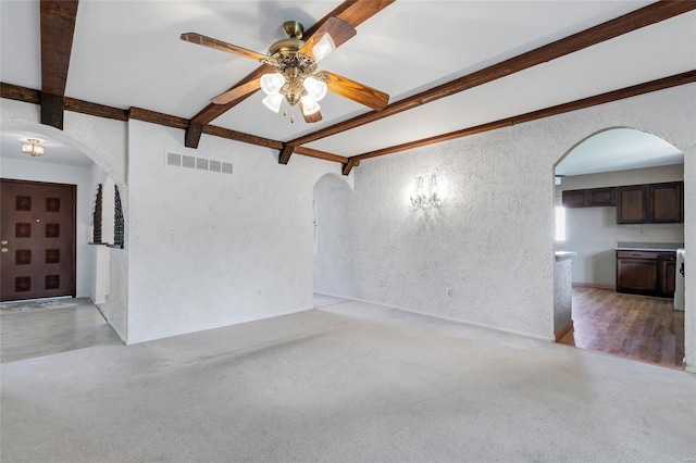 empty room featuring visible vents, arched walkways, a ceiling fan, a textured wall, and beam ceiling