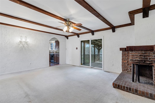 unfurnished living room featuring ceiling fan, beamed ceiling, arched walkways, a brick fireplace, and a textured wall
