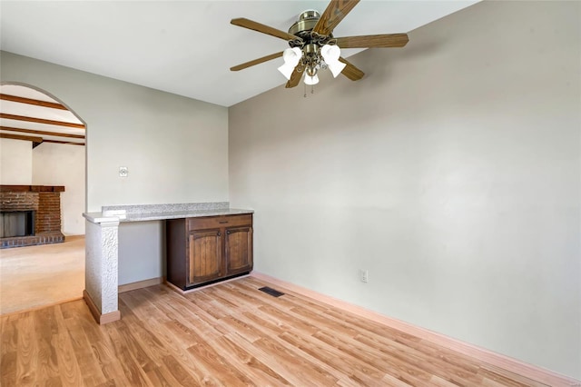 interior space with a fireplace, arched walkways, a ceiling fan, visible vents, and light wood finished floors