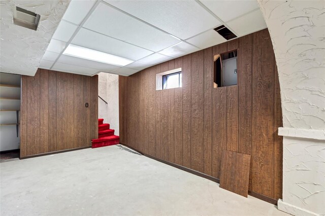 finished below grade area featuring stairway, wooden walls, and a drop ceiling