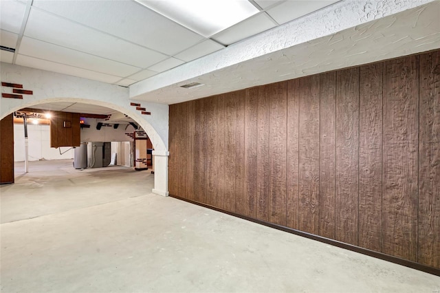 below grade area with wood walls, a drop ceiling, and arched walkways