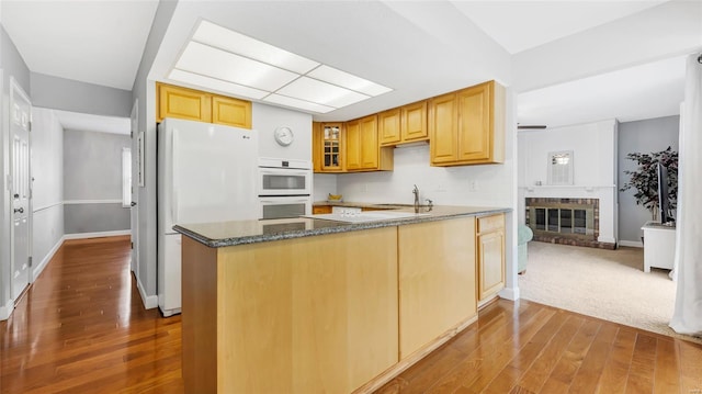 kitchen with a peninsula, dark wood finished floors, glass insert cabinets, and white appliances