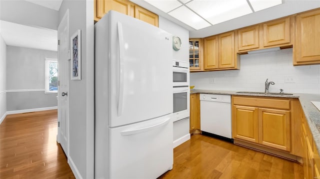 kitchen featuring light wood-style floors, white appliances, glass insert cabinets, a sink, and backsplash