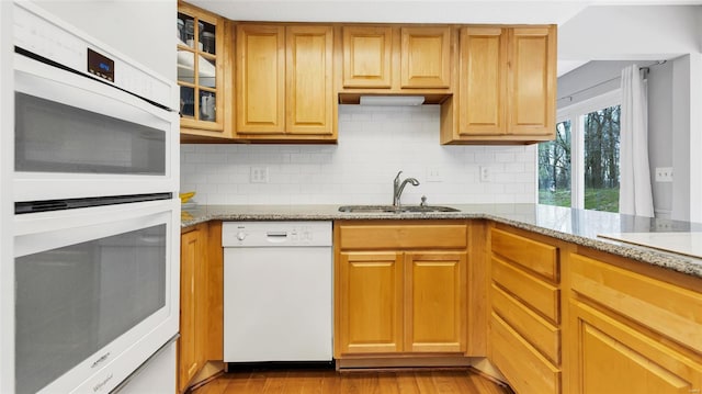 kitchen with white appliances, light wood-type flooring, a sink, and light stone counters