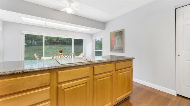 kitchen featuring stone counters, baseboards, a ceiling fan, and wood finished floors