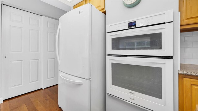 kitchen with white appliances, wood finished floors, and light stone countertops