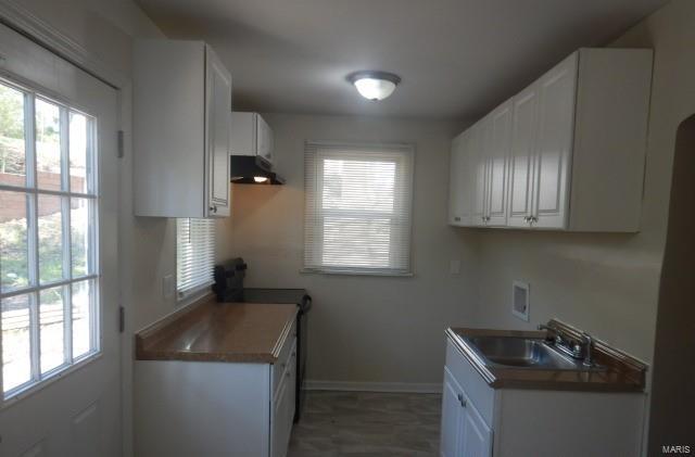 kitchen featuring a healthy amount of sunlight, a sink, white cabinetry, and baseboards