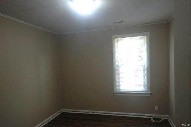 empty room featuring dark wood-style flooring, visible vents, baseboards, and crown molding