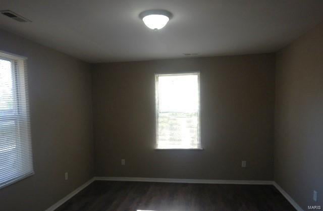 empty room with dark wood-style floors, baseboards, and visible vents