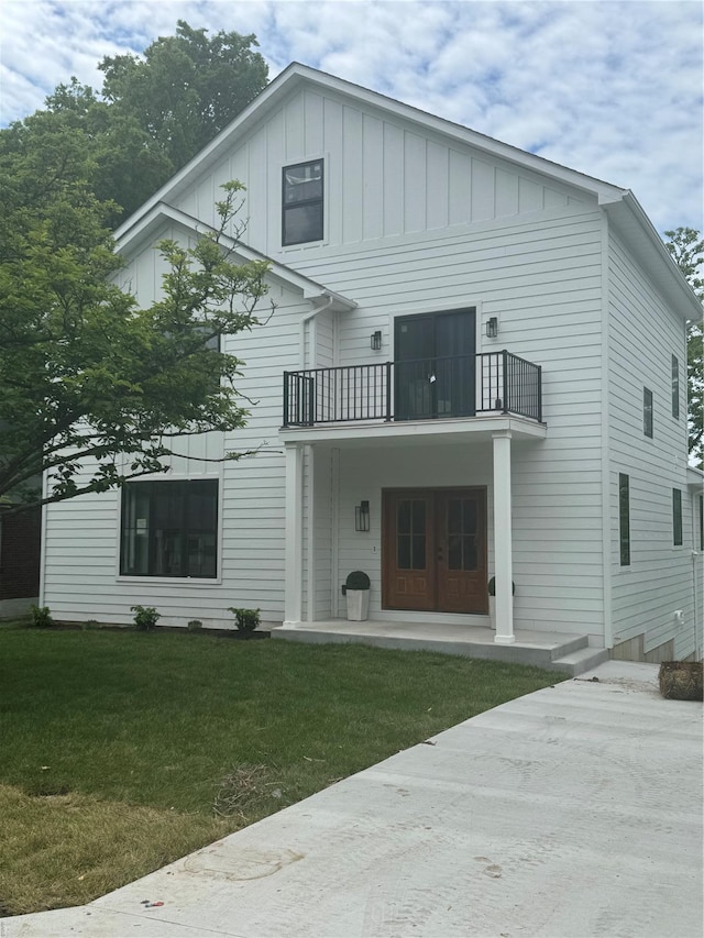 back of property with a balcony, board and batten siding, and a yard