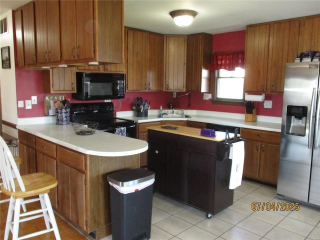 kitchen featuring a peninsula, light countertops, black appliances, brown cabinetry, and a sink