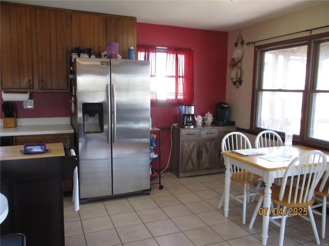 kitchen featuring stainless steel refrigerator with ice dispenser, brown cabinets, light countertops, and light tile patterned flooring