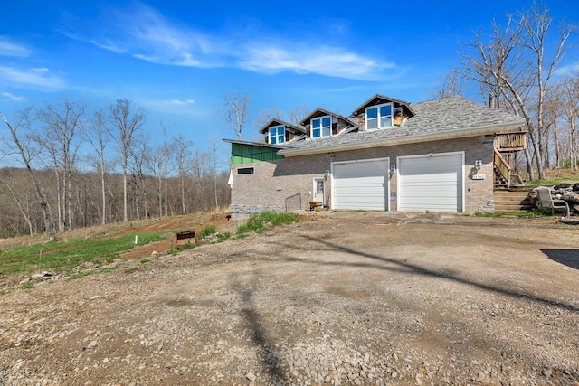 view of side of property featuring brick siding, driveway, stairway, and a garage